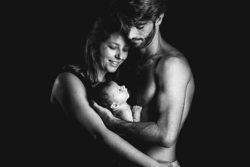 Photo de bébé nouveau né avec ses parents papa et maman en noir et blanc en studio en low key