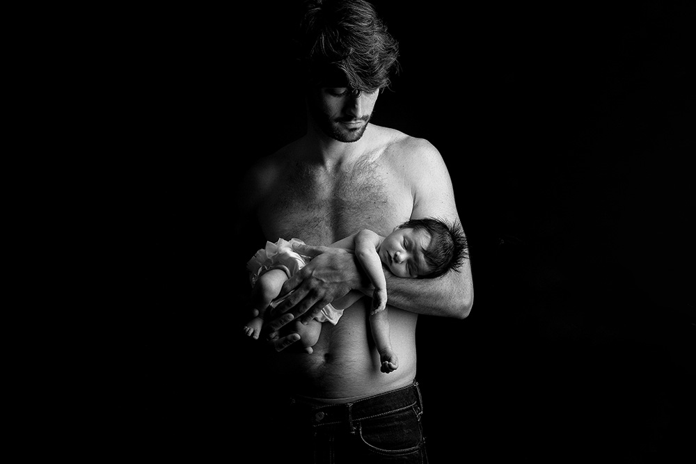 Photo de bébé nouveau né avec papa en noir et blanc en studio en low key
